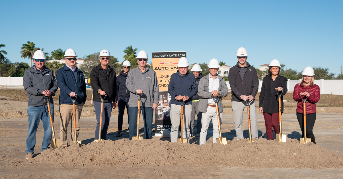 Group wearing white hard hats holding gold shovels during a groundbreaking ceremony.