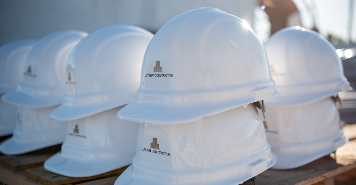 White Lutgert Construction hard hats stacked on a wooden pallet at a construction site.