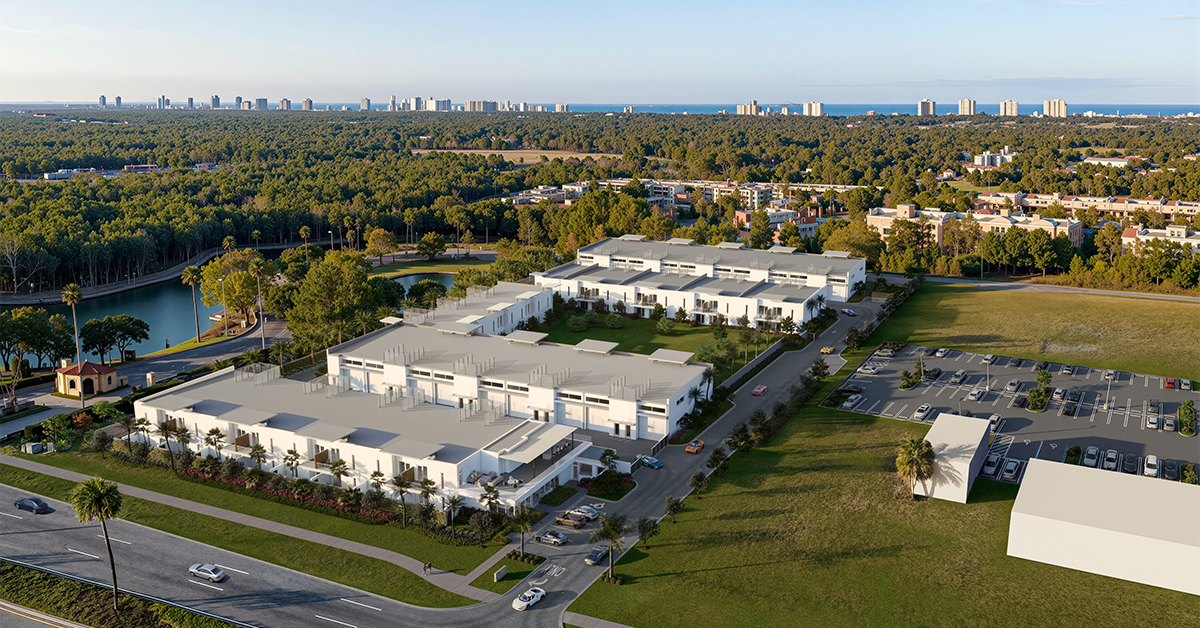 Aerial view of modern auto storage complex with palm trees, parking lot, and distant coastal skyline.