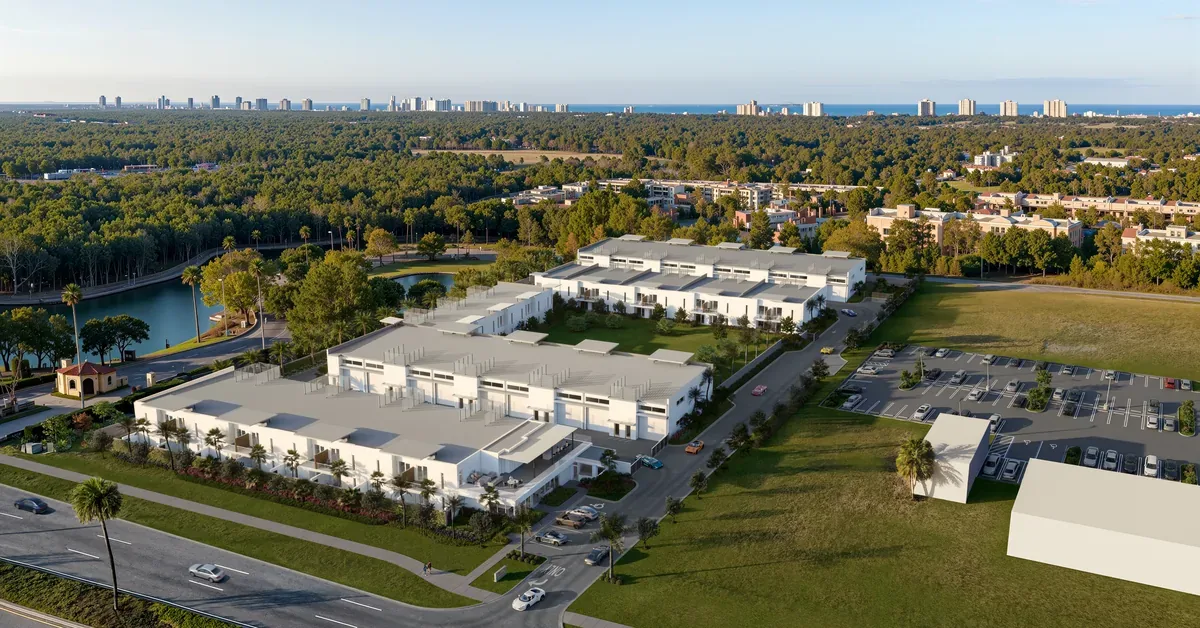 Aerial view of a modern white industrial flex-space development surrounded by lush greenery, with a coastal city skyline visible in the distance.